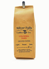 Load image into Gallery viewer, A 12 oz bag of Silver Falls Coffee Co. Colombia Dark Ground Coffee in a brown kraft paper bag with a metal clip at the top, shown against a plain white background.